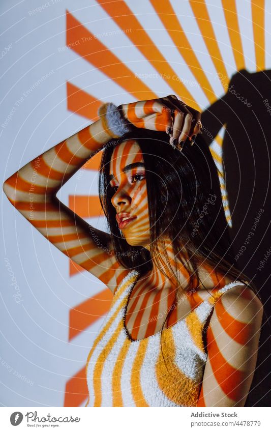 Trendy Hispanic model touching hair in projector light touch hair cool trendy individuality confident stare stripe woman portrait millennial contrast orange