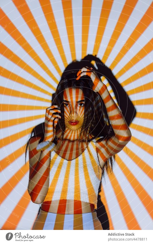 Trendy Hispanic model touching hair in projector light touch hair cool trendy individuality confident stare stripe woman portrait millennial contrast orange