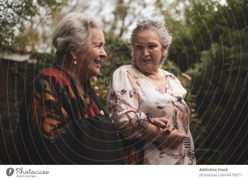 Cheerful senior women in garden old elderly generation retire together friend happy communicate pensioner spend time bush female rose talk flower summer stroll