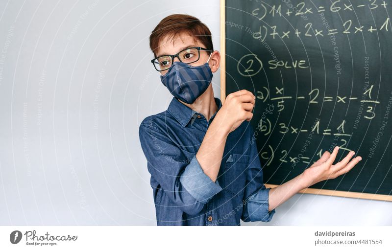 Boy with mask solving math exercises on blackboard boy face mask school coronavirus math class new normal explaining equations safety copy space people student