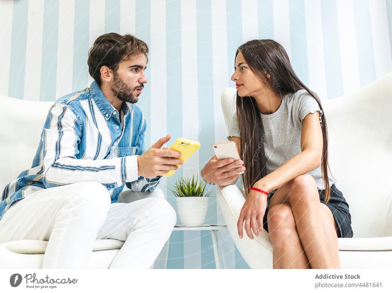 Man and woman with smartphones sitting on armchairs cellphone together content communicate talk using elegant gadget style browsing male white female furniture