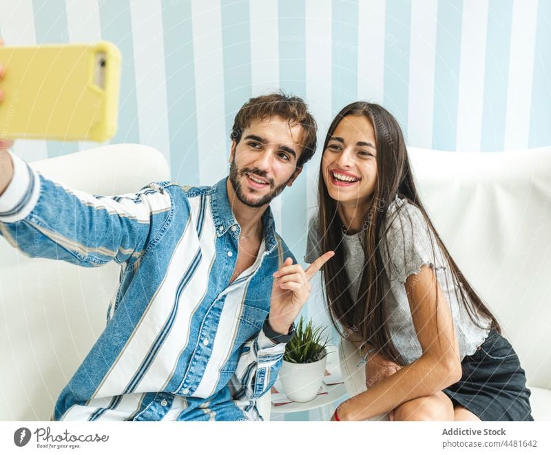 Cheerful couple taking selfie on armchairs smartphone cellphone self portrait together content using positive gadget style smile cheerful beard brunette