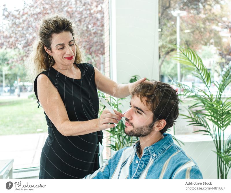 Woman cutting male client in salon woman barber customer master hairstylist service beard window content female style professional tool process smile positive