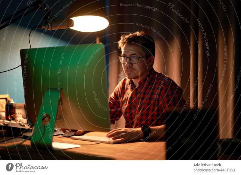 Focused man working on computer in dark studio concentrate podcast record sound engineer microphone job radio using male young checkered shirt eyeglasses