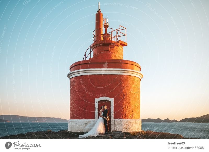 Lighthouse with a just married couple on its door wedding husband wife apparel love copy space lighthouse ocean sea heterosexual bride groom sunset portrait