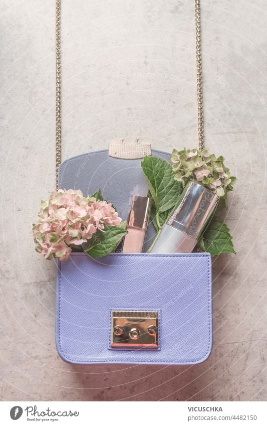 Purple handbag with hydrangea flowers and cosmetic products on pale grey concrete table. Lifestyle concept. Top view. purple lifestyle top view accessories