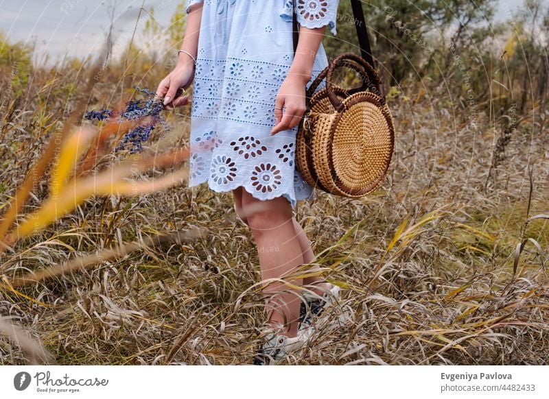 Woman with trendy nude rattan round bag and flowers walking outdoors. Village landscaped, fall season. fashion wicker beautiful lady woman village boho style