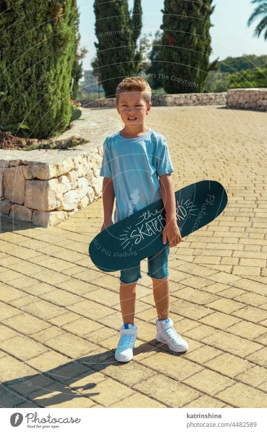 Preschooler boy keep a skateboard in hands in park child sport summer kid family mockup nature lifestyle leisure outdoor t-shirt young skater fun active