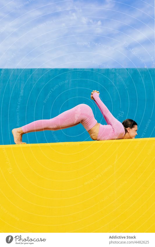 Slim female doing yoga asana on blue and yellow background woman stretch flexible practice balance wellness leg raised posture wellbeing pose mindfulness
