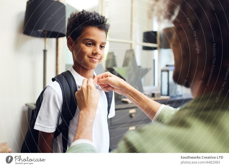 Boy smiling as father buttons his shirt school mixed race boy smile help son prepare assistance indoors day home interior two people portrait authentic