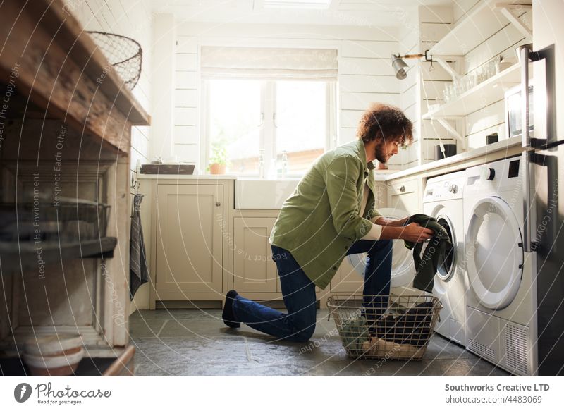 Man loading washing machine in kitchen mixed race man one adult indoors lifestyle interior chores day home alone authentic tumble dryer room appliance domestic