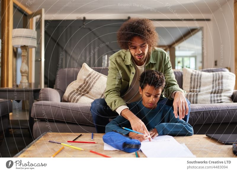 Father helping son draw at home mixed race father boy child concentrate portrait bonding indoors day interior two people authentic relax childhood leisure