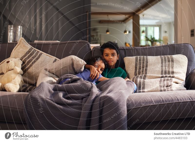 Two boys cuddling on sofa under blanket mixed race two cuddle child brother care love together indoors day home interior people portrait authentic content enjoy