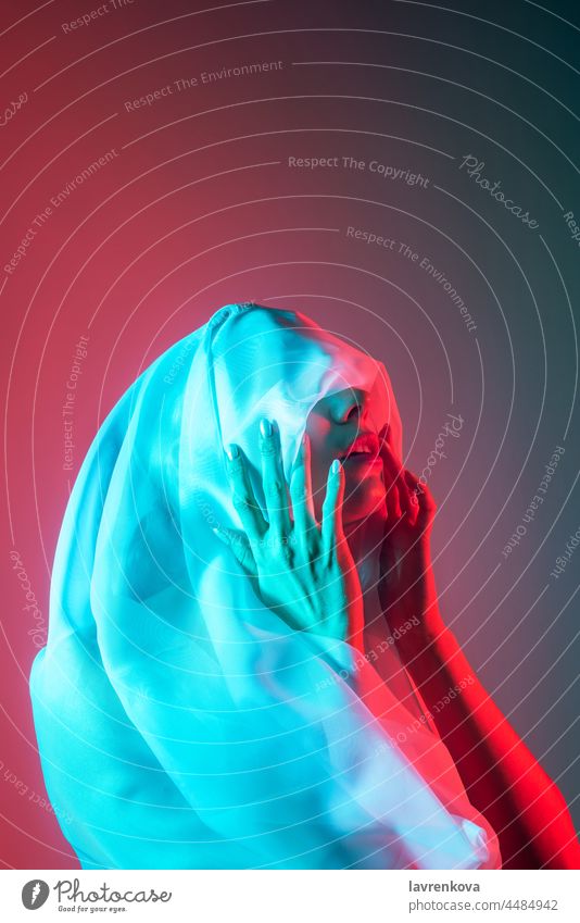 Studio portrait of woman with her face covered in neon blue and red lightning cloth model artistic dark alone hipster cool stylish retro bright night studio