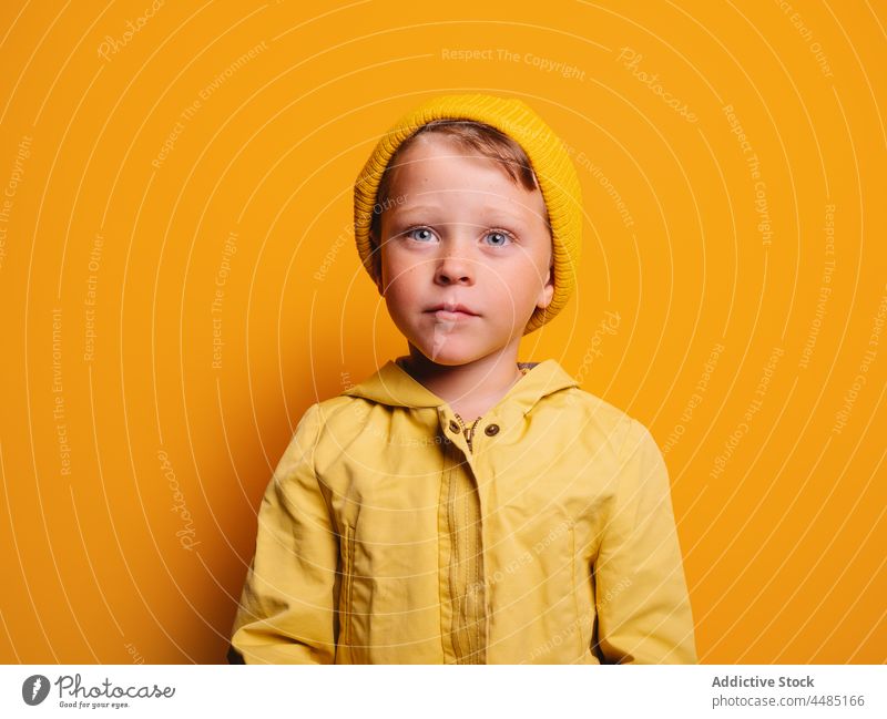 Calm boy in trendy outfit standing against yellow background calm childhood style individuality wear kid raincoat comfort zone pleasure little color cloth vivid