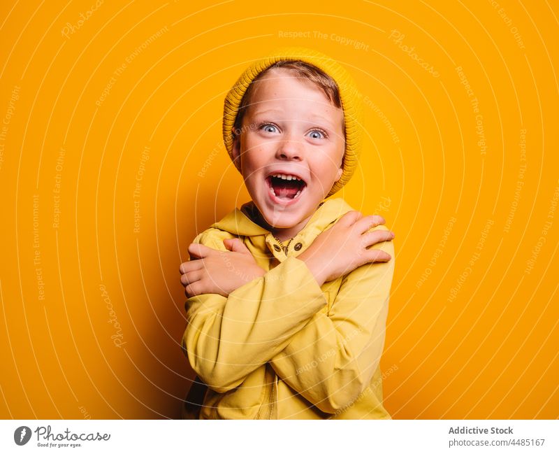 Happy smiling boy in trendy outfit standing with crossed arms against yellow background hug calm embrace childhood style individuality arms crossed wear