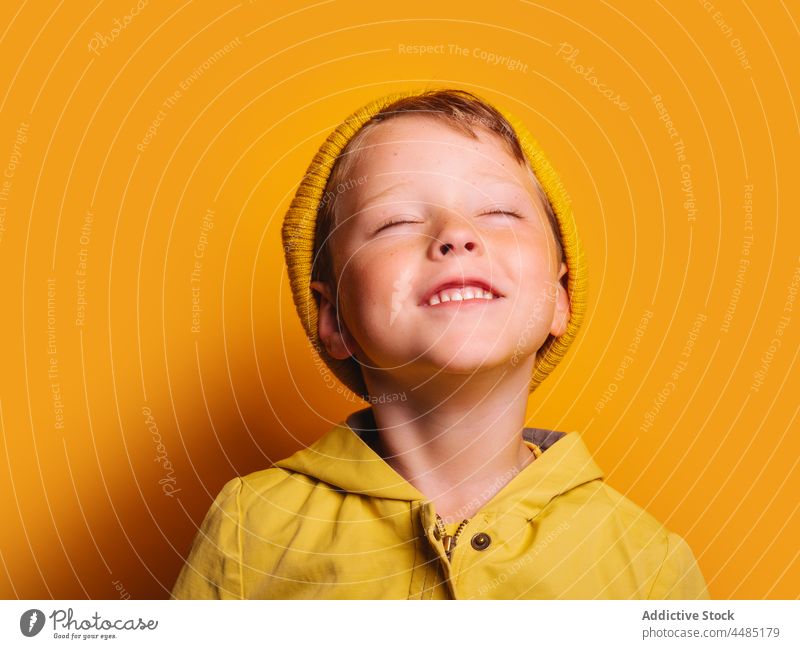 Laughing boy with eyes closed against yellow background happy laugh cheerful autumn portrait jacket outerwear beanie glad joy style kid trendy child bright