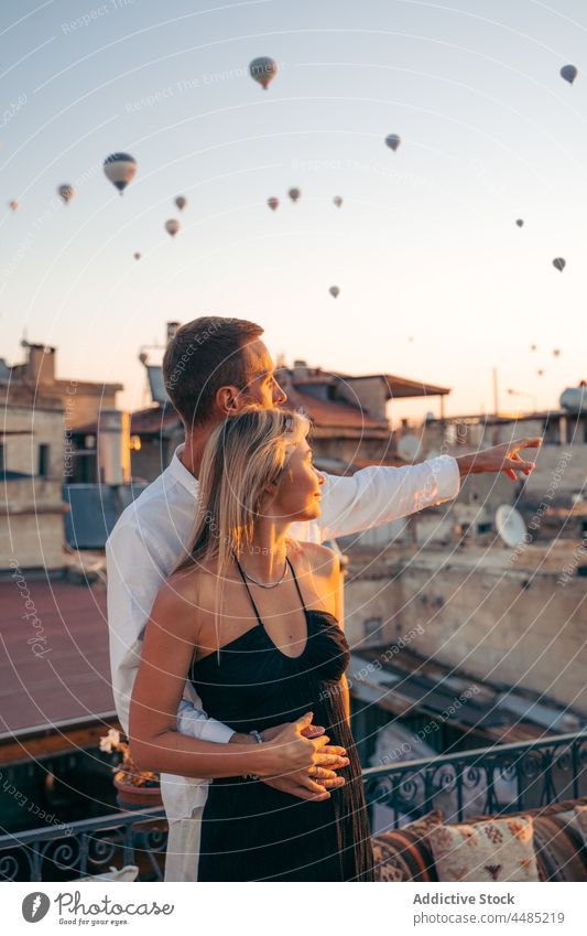 Husband pointing away while hugging wife on terrace couple embrace soulmate admire together rooftop date romantic point away air balloon love relationship