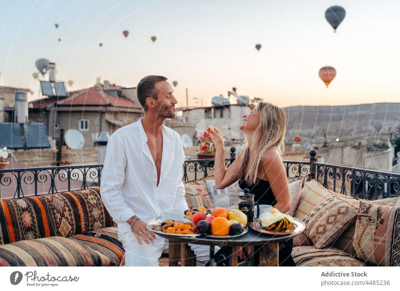 Happy couple on rooftop against hot air balloons date romantic together affection sunset sundown relationship holding hands twilight romance bonding vacation