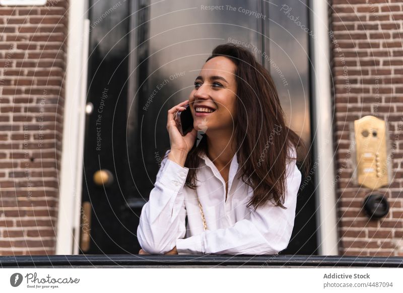 Smiling woman making a phone call on street building smartphone entrance happy smile device using gadget female browsing online mobile urban young handrail