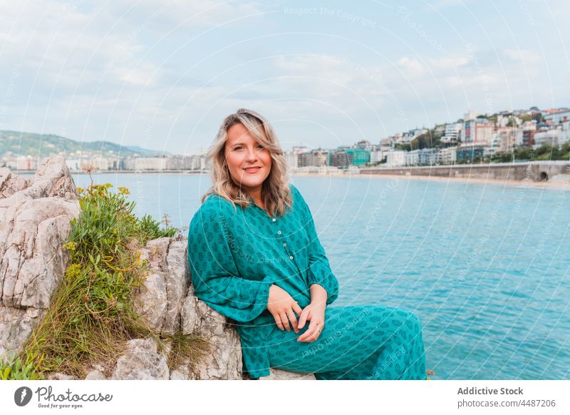 Dreamy woman sitting on rocks with green plants close to the sea style nature positive dreamy adjust environment female donostia trendy san sebastian charming