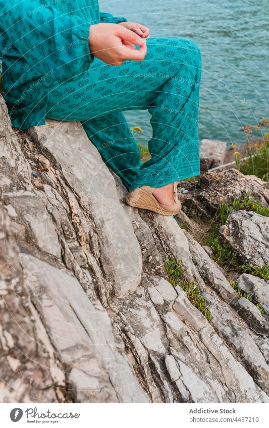 Anonymous cheerful woman sitting on stone against ocean and green hills style border rock harmony female spain san sebastian basque country bay of biscay water