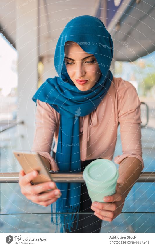 Muslim woman with takeaway coffee and smartphone city browsing hijab mobile female ethnic arab muslim street online message internet surfing device beverage