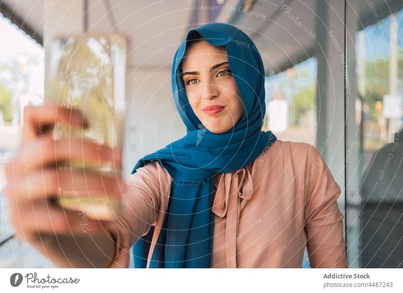 Smiling Muslim woman taking selfie in city smartphone hijab takeaway self portrait smile tradition female arab ethnic muslim street headscarf happy using gadget