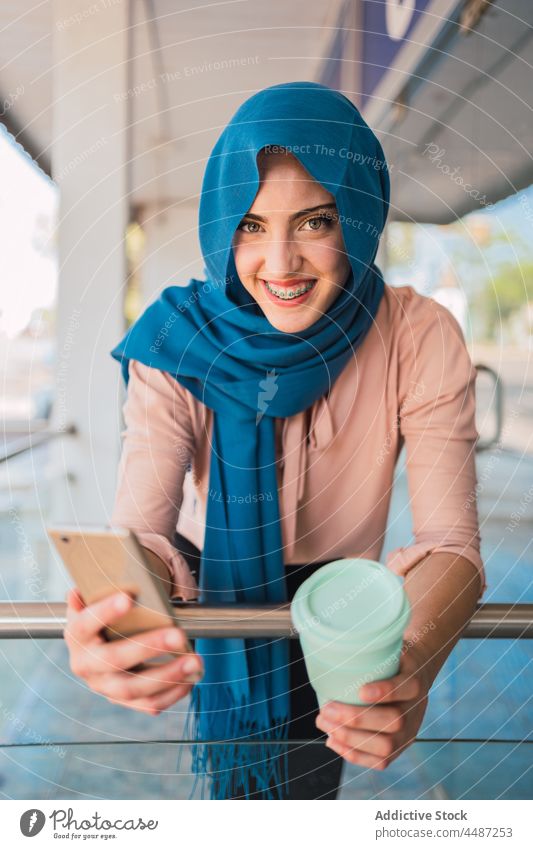 Muslim woman with takeaway coffee and smartphone city browsing hijab smile mobile female ethnic arab muslim street online message internet cheerful surfing