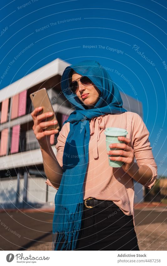 Stylish Muslim woman browsing smartphone in city message hijab coffee takeaway using social media cellphone female ethnic arab muslim style mobile street
