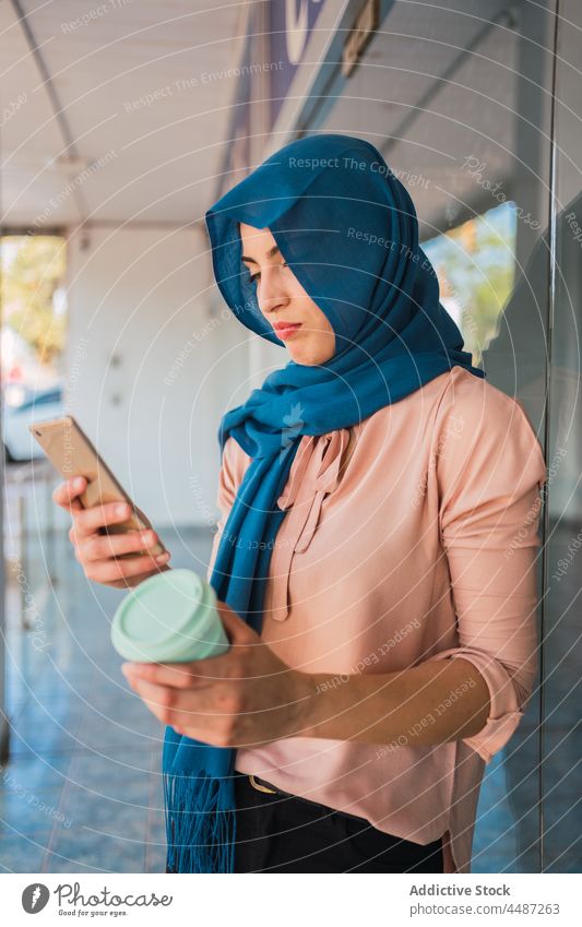 Muslim woman with takeaway coffee and smartphone city browsing hijab mobile female ethnic arab muslim street online message internet surfing device beverage
