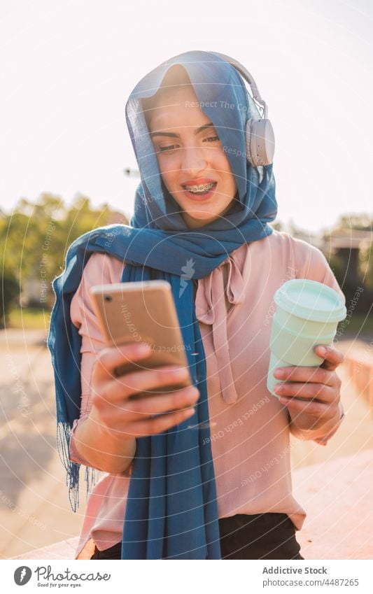 Muslim woman surfing Internet on smartphone in city listen music headphones hijab using browsing headscarf female muslim arab ethnic meloman gadget tune