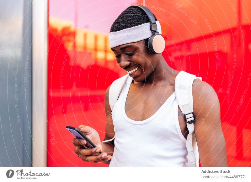 Black man in headphones browsing smartphone in street listen music message happy positive glad using city content wireless african american ethnic black gadget