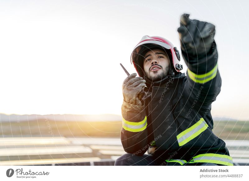 Young fireman speaking into transmitter firefighter helmet uniform report walkie talkie professional occupation job career glove positive male safety confident
