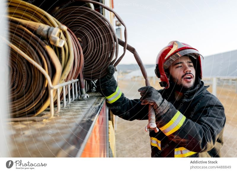Firefighter pulling a fire hose from the truck firefighter fireman hardhat farmland helmet equipment rescue countryside occupation profession uniform safety