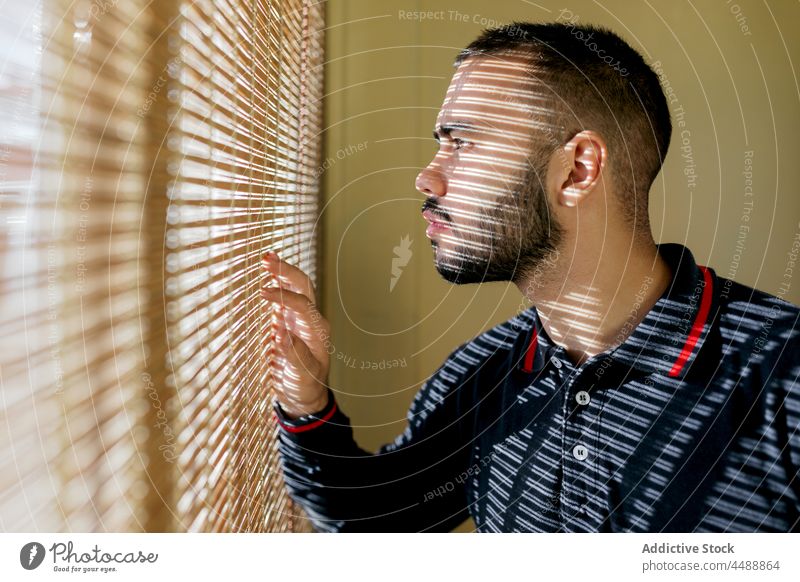 Man looking out window man fireman firefighter beard confident calm sweat jacket station occupation profession unshaven young sporty male sunlight blind blinds