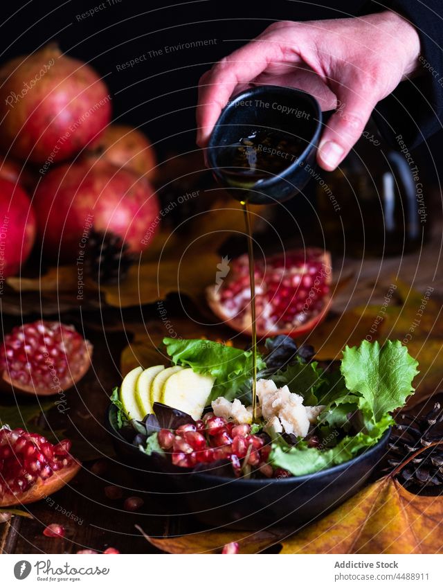 Cook pouring olive oil in bowl with pomegranate salad cook add dish vegetarian chef bottle culinary meal serve delicious food table cuisine autumn leaf fall