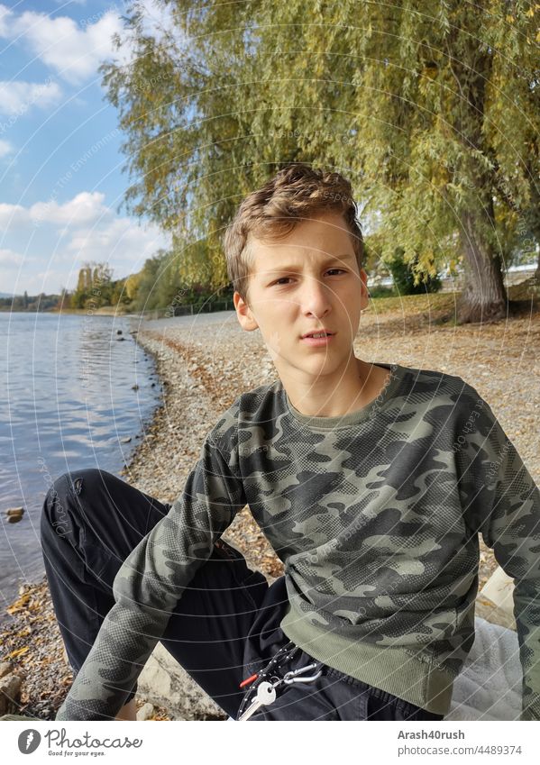 Rascal with a sceptical look Boy (child) teenager by the lake Exterior shot chilly Skeptical Front view bank Lake Water Nature Colour photo Relaxation Calm