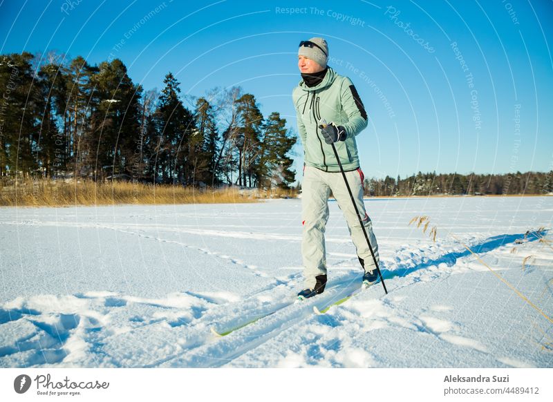 Winter sport in Finland - cross-country skiing. Handsome fit man skiing in sunny winter. Frozen lake and forest covered with snow. Active people outdoors. Scenic peaceful Finnish landscape.