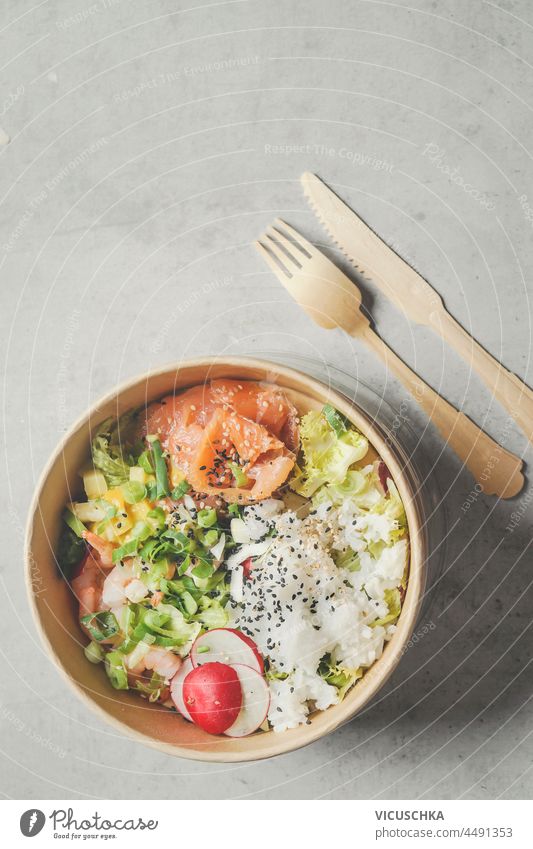 Modern sustainable food delivery with eco friendly packaging and cutlery. Healthy Asian take away food : salad bowl with salmon on grey concrete kitchen table. Top view.