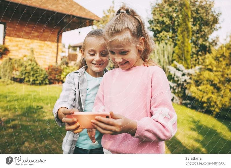 Two little girls outside their house are talking on a mobile phone with friends or parents via video link. selfie kids smartphone adoption people education