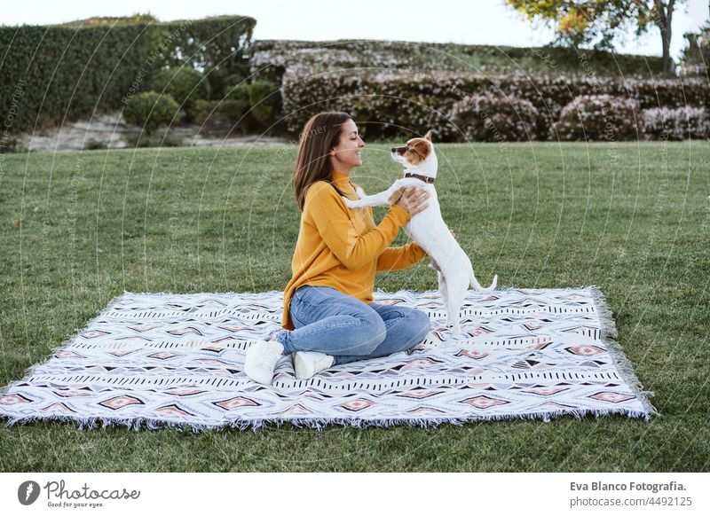 woman having fun with jack russell dog in park, sitting on blanket during autumn season. Pets and love concept happy kiss enjoy plaid lick together caucasian