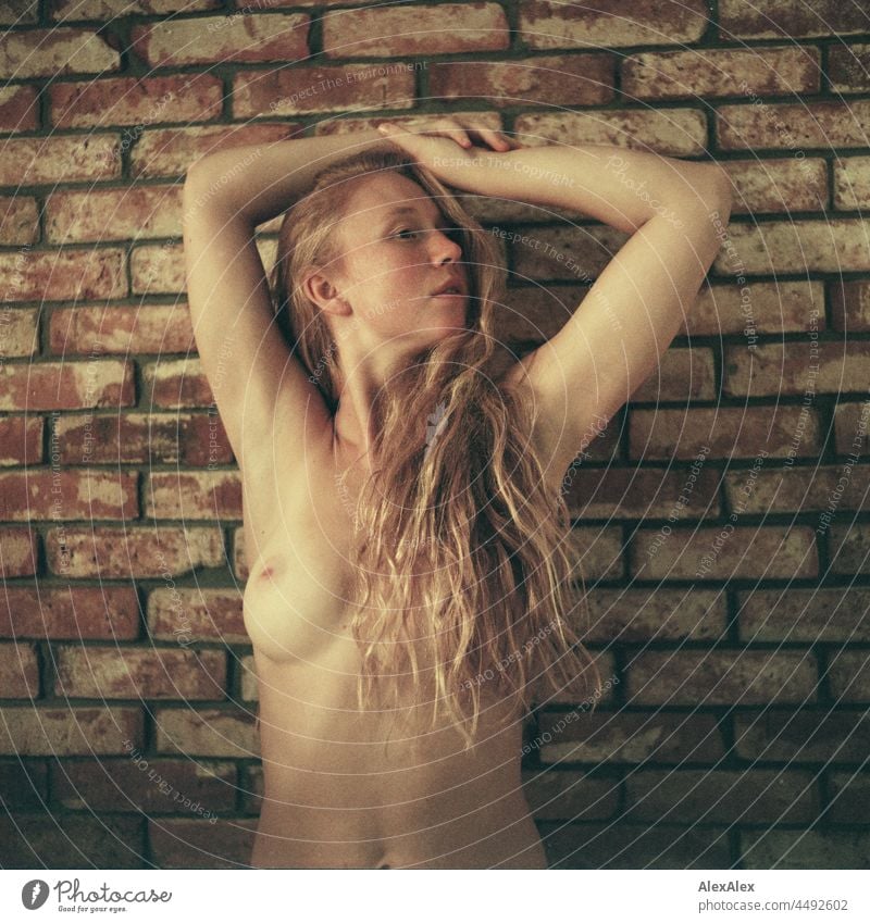 analogue nude portrait of a young woman with freckles and red hair, standing in front of a brick wall with her arms crossed over her head Emanation tranquillity
