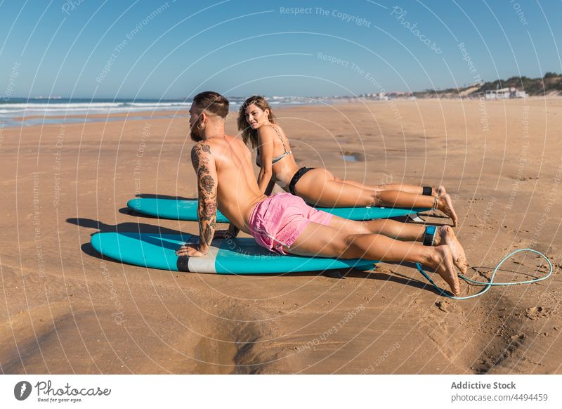 Sportive couple warming up on surfboards on coast sportspeople surfer beach hobby warm up stretch prepare water sports seaside swimwear woman summer equipment
