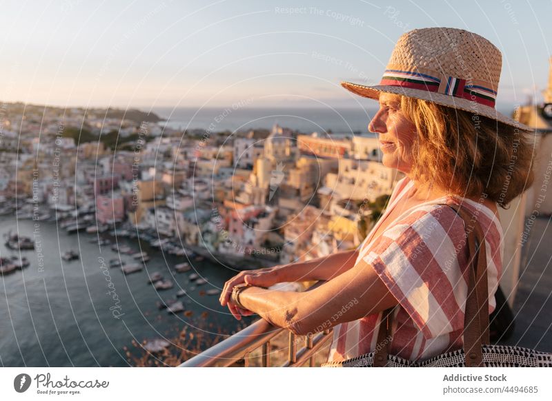 Happy female traveler admiring coastal town and sea at sunset woman admire island tourist vacation peaceful picturesque scenic sundown summer dress straw hat