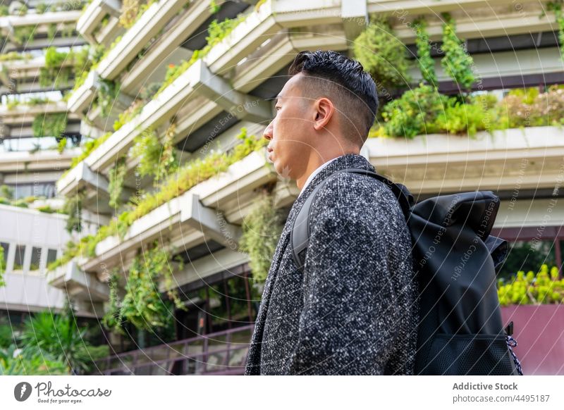 Stylish Asian businessman with backpack against contemporary buildings in city entrepreneur well dressed rucksack contemplate haircut modern natural style