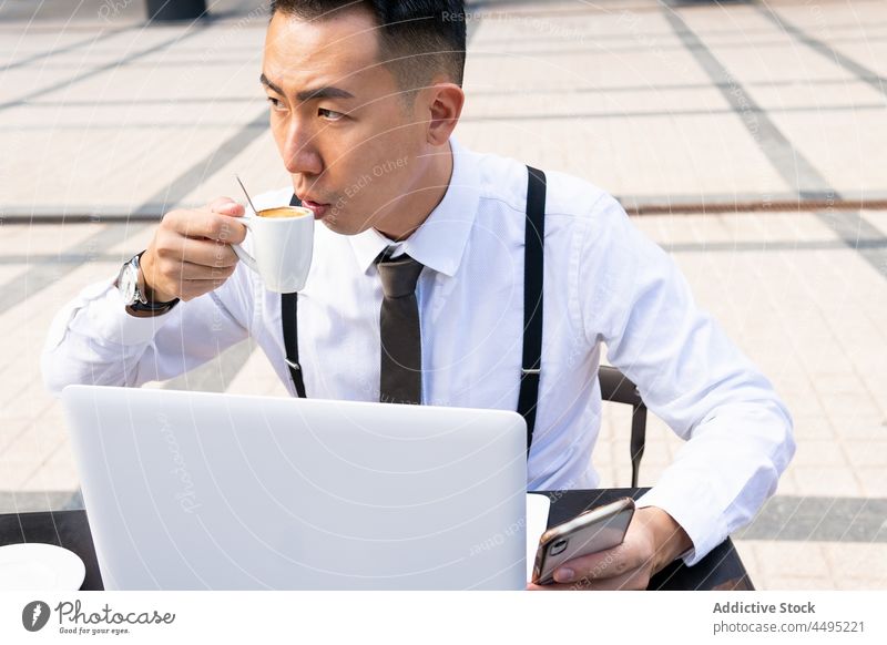 Contemplative ethnic businessman with coffee and laptop in street cafe entrepreneur wistful hot drink beverage building city internet online gadget device