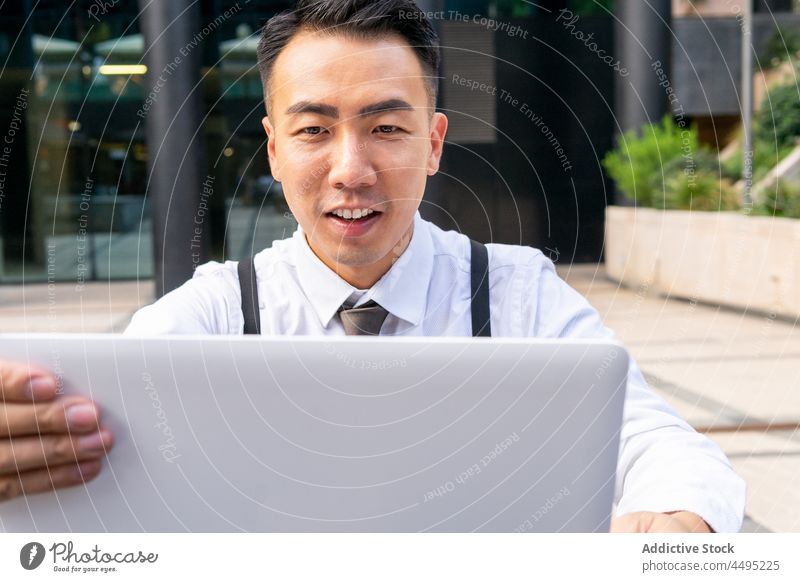 Stylish Asian businessman working on laptop in city cafe entrepreneur coffee internet online using gadget device building modern self employed street formal