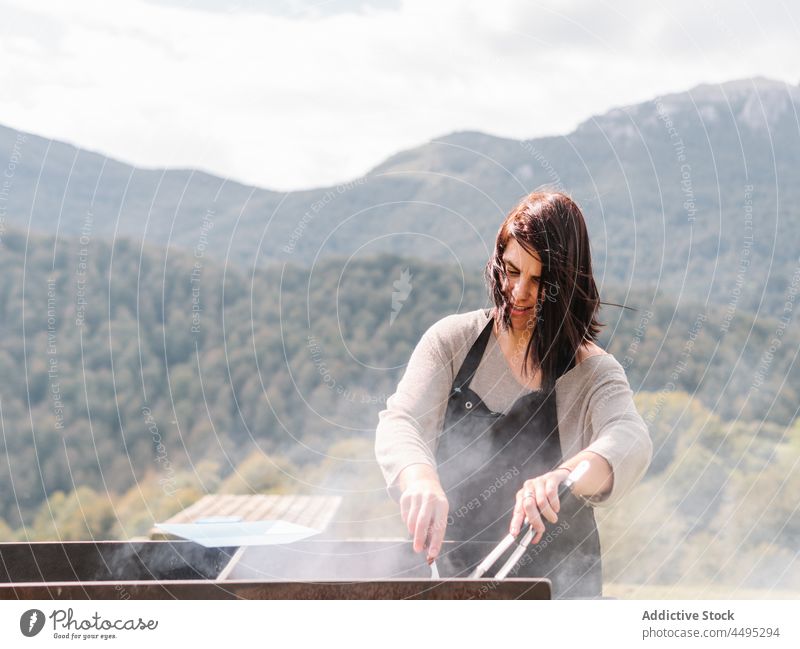 Woman roasting sausages on grill in countryside woman cook meat barbecue grate field bbq food tasty summer chef delicious picnic hot various assorted tong