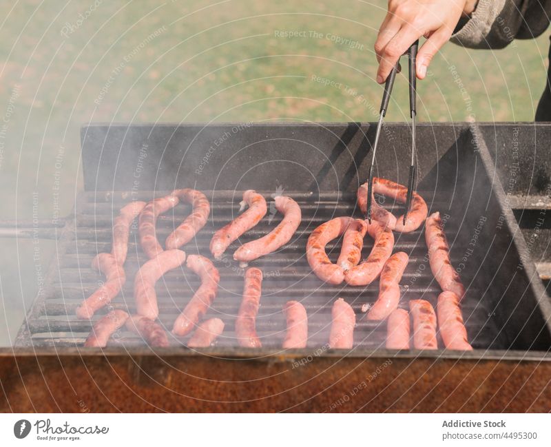 Anonymous person frying sausages on grill in countryside meat barbecue roast charcoal grate bbq food tasty summer delicious picnic yummy fresh hot various